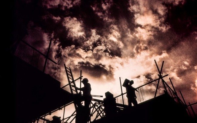 workers on building site silhouetted against red cloudy sky