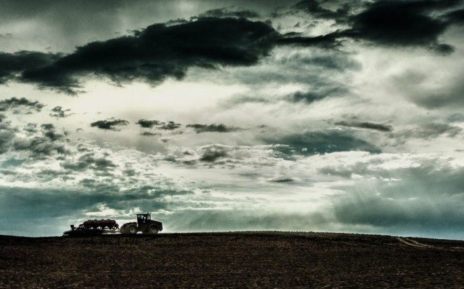 tractor ploughing fields silhouetted against stormy sky